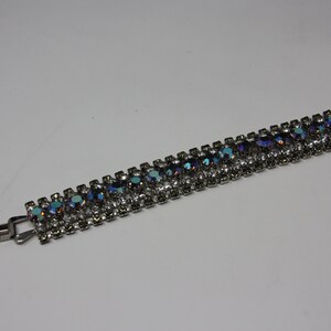 May include: A silver bracelet with a row of iridescent blue and clear rhinestones.