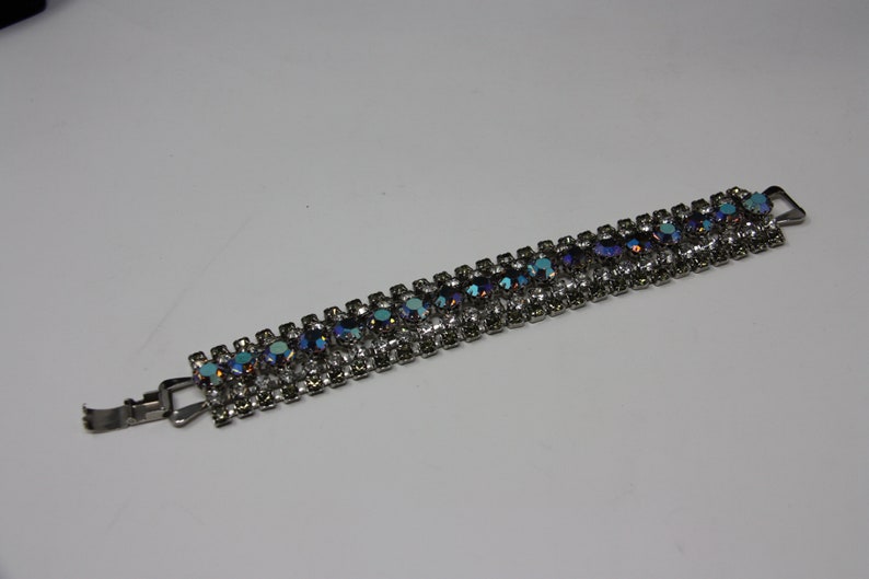 May include: A silver bracelet with a row of iridescent blue and clear rhinestones.