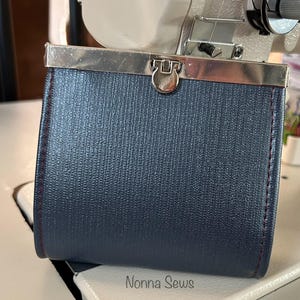 May include: A dark blue coin purse with a silver metal frame and a silver clasp. The purse has red stitching around the edges.