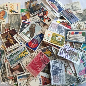 May include: A collection of vintage US postage stamps featuring a variety of designs, including a  'Special Olympics' stamp, a 'US Bicentennial' stamp, and a 'Plant for More Beautiful Highways' stamp. The stamps are in various colors and sizes.