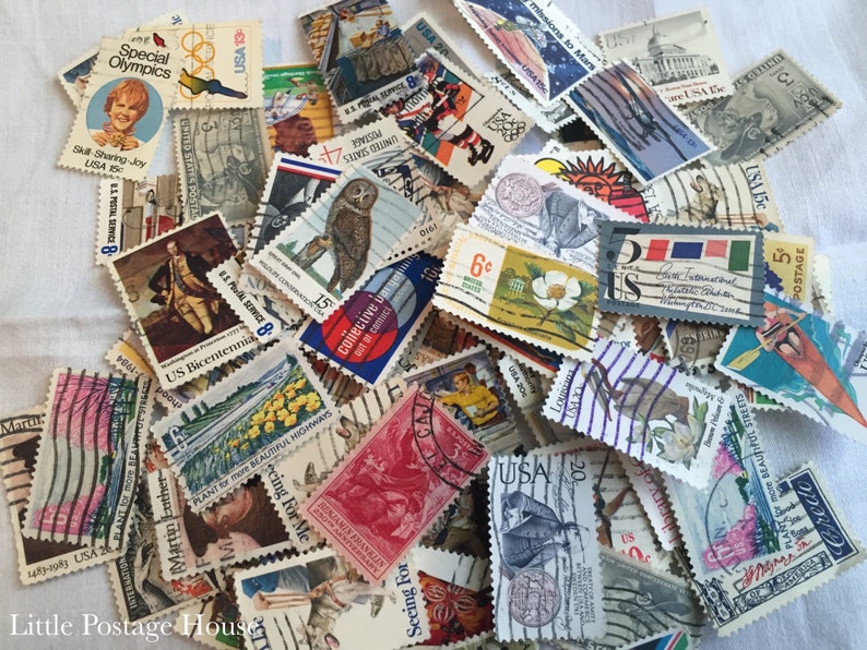 May include: A collection of vintage US postage stamps featuring a variety of designs, including a  'Special Olympics' stamp, a 'US Bicentennial' stamp, and a 'Plant for More Beautiful Highways' stamp. The stamps are in various colors and sizes.