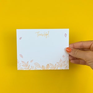 May include: A white card with the word "Thankful" written in orange script. The card has a border of orange leaves around the bottom edge.