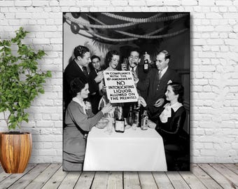 May include: A black and white photo of a group of people gathered around a table. A sign reads "In compliance with the 18th Amendment, No Intoxicating Liquor Allowed on the Premises".