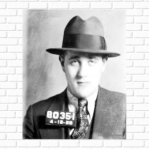 May include: Black and white mugshot of a man wearing a fedora and a suit. The mugshot has a number "80351" and the date "4-12-28" printed on it. The text "Ferris Trading Company" is printed at the bottom of the mugshot.