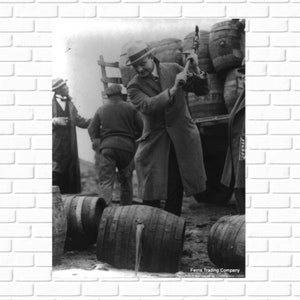 May include: Black and white photo of a man in a hat using a mallet to break open a barrel. The barrel is on the ground and there are other barrels in the background. The text at the bottom of the photo reads 