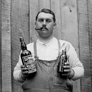 May include: A black and white photo of a person holding two bottles of alcohol. One bottle is labeled 