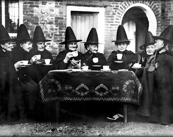 May include: A group of women wearing black cloaks and tall pointed hats are gathered around a table, having tea. They are all smiling and appear to be enjoying themselves.