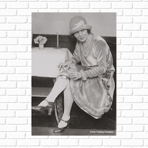 May include: A woman in a velvet dress and hat sits on a chair with her legs crossed. She is holding a small object in her hand. The image is in black and white and has the text 