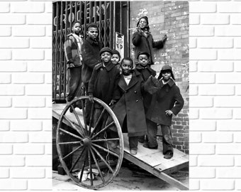 May include: A group of young boys stand in front of a building with a sign that reads "Grocery". The boys are wearing coats and hats. One boy is holding a large wooden wheel.