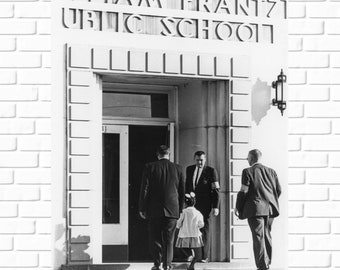 May include: A black and white photo of a school entrance with the words "I AM FRANTZ PUBLIC SCHOOL" above the doorway. Three adults and a child are walking through the doorway.