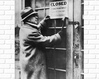 May include: A black and white photo of a man in a coat closing a door with a sign that reads "Closed for the violation of the National Prohibition Act, in order of the United States District Court, United States Marshal."