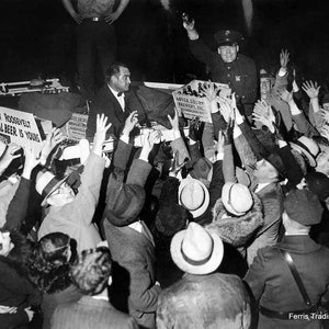 May include: A black and white photo of a crowd of people gathered around a man holding a sign that reads 