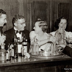 May include: A black and white photo of four people sitting at a bar. There are several bottles and glasses on the bar. The text 