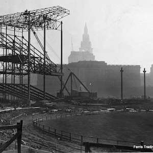 May include: A black and white photo of a stadium under construction. The steel framework of the stadium is visible, along with a crane and other construction equipment. The city skyline is visible in the background.