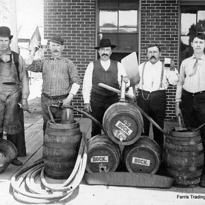 May include: Five men stand in front of a brick building with five barrels of beer. The barrels are labeled 