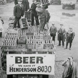 A vintage black and white photograph of men in flat caps and coats loading crates of beer onto a truck in Cleveland, Ohio. A large banner on the back of the truck reads "BEER" Call WE HAVE IT HENDERSON 8030.