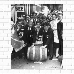 May include: A black and white photo of a group of people gathered around a barrel. The people are all smiling and holding drinks. The barrel is labeled 