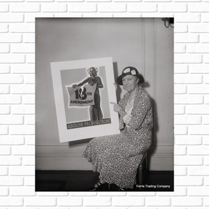 May include: A black and white photo of a woman sitting on a chair holding a poster that reads 