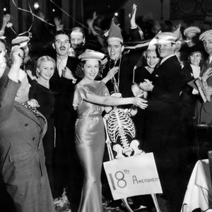 May include: A group of people celebrating the repeal of the 18th Amendment, also known as Prohibition. The people are dressed in formal attire and are holding glasses of champagne. There is a sign in the foreground that reads 
