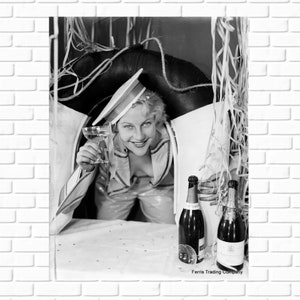 May include: A black and white photo of a woman in a sailor hat holding a glass of champagne. She is standing behind a life preserver and there are two bottles of champagne in the foreground. The text at the bottom of the image reads 