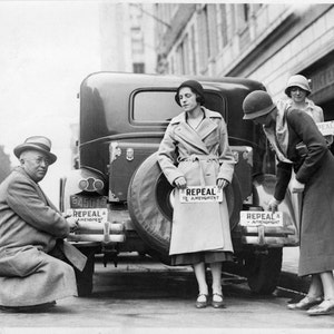 May include: Three people stand near a black car with signs that read 