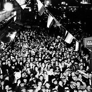 May include: A black and white photo of a large crowd of people gathered in front of a subway entrance. The crowd is cheering and waving their arms in the air. There are flags hanging from the entrance. The sign above the entrance reads 