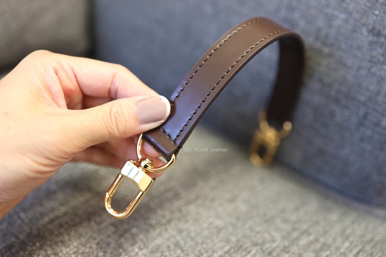 May include: A brown leather strap with gold-toned hardware. The strap is stitched with a decorative stitch and has a swivel hook on one end.