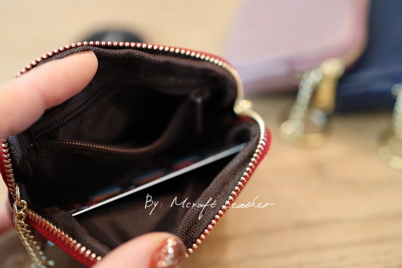 Puede incluir: Una bolsa de cuero rojo con cremallera y forro marr&oacute;n. La bolsa est&aacute; abierta y se puede ver una tarjeta en el interior. El texto "By: Mcraft Leather" est&aacute; impreso en la bolsa.