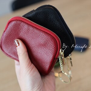 Puede incluir: Dos peque&ntilde;as carteras con cremallera, una roja y otra negra, con una cadena dorada y un llavero. Las carteras son de cuero y tienen una superficie texturizada. Por: Mcraft Leather.