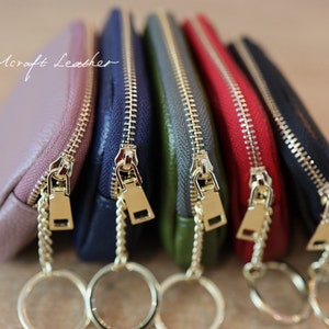 Puede incluir: Cinco peque&ntilde;as bolsas con cremallera de color dorado y llaveros. Las bolsas son de color rosa, azul, verde, rojo y negro. El texto "By: Mcraft Leather" es visible en la bolsa superior.