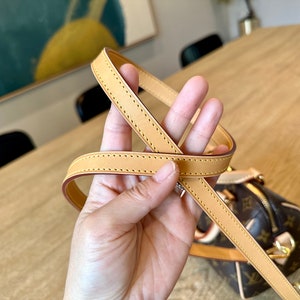 May include: Tan leather handbag strap with a stitched design. The strap is attached to a brown and tan patterned handbag with gold-colored hardware. The bag has a zipper closure.