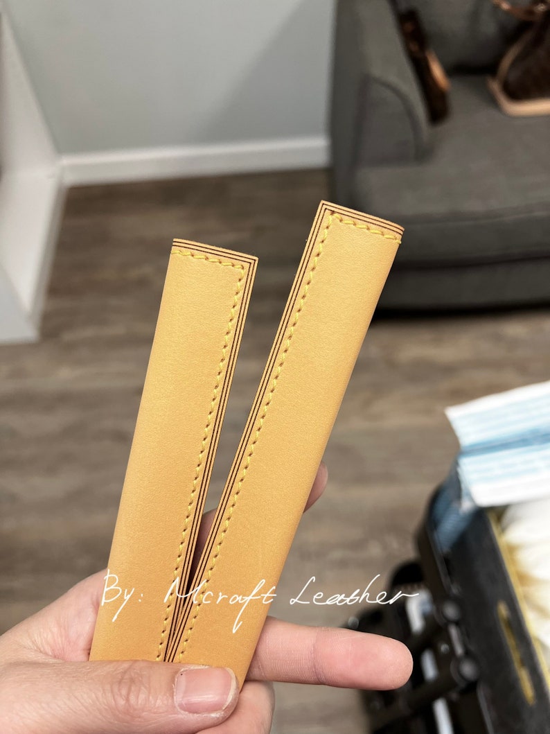 May include: Two pieces of yellow leather with a stitched edge. The leather is folded in half and the stitching is visible on both sides. The text "By: Microft Leather" is visible on the leather.