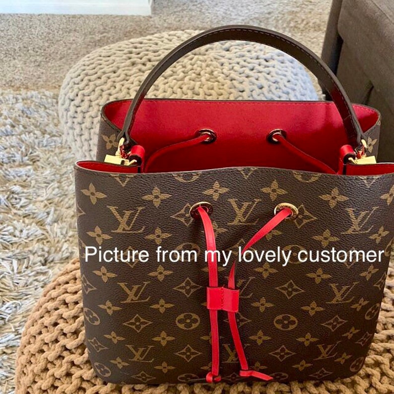 May include: A brown and tan monogrammed leather bucket bag with a red drawstring and gold hardware. The bag has a red leather lining.