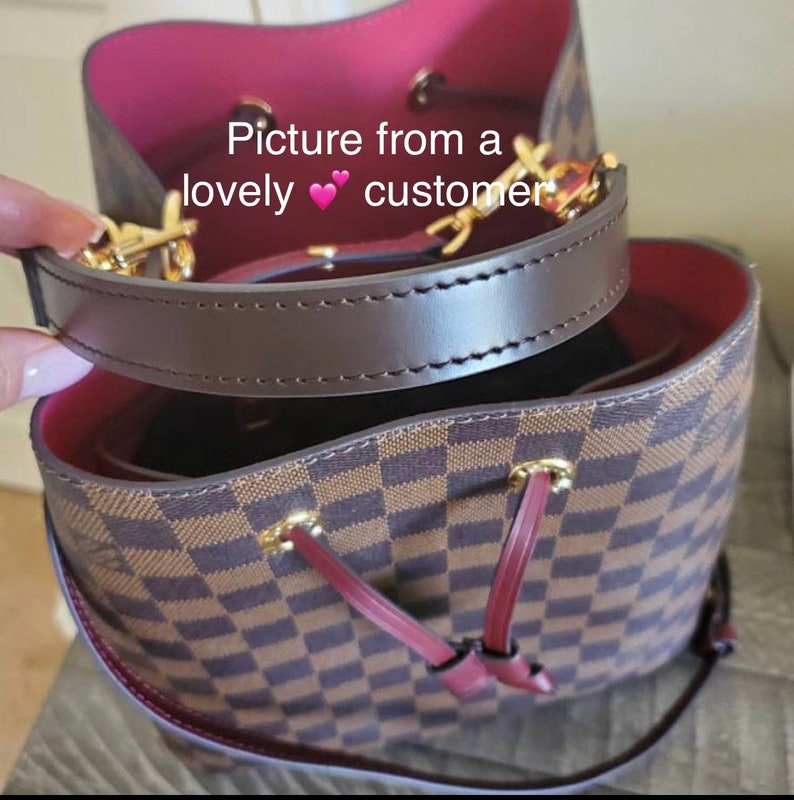 May include: A brown and black checkered handbag with a brown leather strap and gold hardware. The bag has a red lining and a drawstring closure.