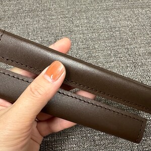 May include: Two brown leather straps with stitching, held in a hand.
