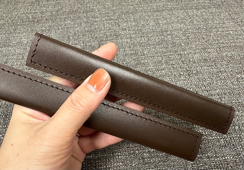 May include: Two brown leather straps with stitching, held in a hand.
