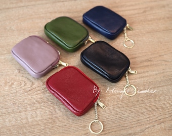 May include: Five small leather coin purses with zipper closures and keychains. The purses are in various colors: purple, green, red, dark blue, and black.