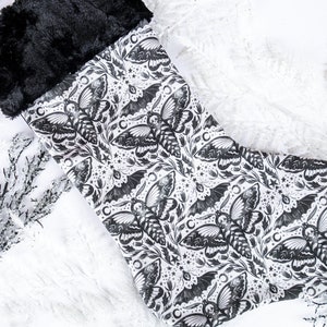 May include: A black and white Christmas stocking with a repeating pattern of moths and bats. The stocking has a black faux fur cuff.