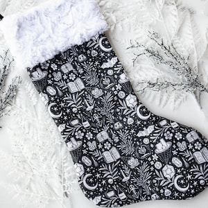 May include: Black and white Christmas stocking with a whimsical design featuring crystals, stars, bats, and other magical elements.