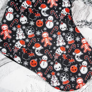 Puede incluir: Una media de Navidad negra con un patr&oacute;n blanco y rojo de calaveras, mu&ntilde;ecos de nieve, bastones de caramelo, murci&eacute;lagos y hombres de jengibre. La media est&aacute; decorada con un tema navide&ntilde;o espeluznante.