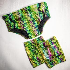 May include: A two-piece swimwear set with a shimmering snakeskin design in green, yellow, and purple. The set comprises high-waisted bottoms and matching shorts, both with black edging.