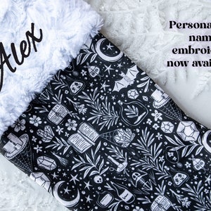 May include: A black and white Christmas stocking with a white faux fur cuff. The stocking features a repeating pattern of moons, stars, crystals, and other witchy imagery. The name "Alex" is embroidered on the cuff in black thread.