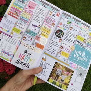 A hand holding a colorful and detailed planners or organizers with various sections for scheduling, reminders, and personal notes.