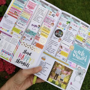 A hand holding a colorful and detailed planners or organizers with various sections for scheduling, reminders, and personal notes.