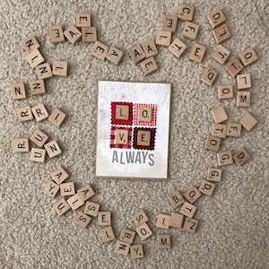 May include: A card with the word "ALWAYS" printed on it. The card is surrounded by letter tiles that spell out "LOVE" in red and white gingham fabric squares.