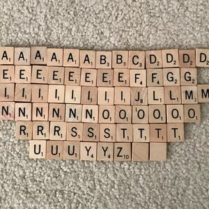 May include: A set of wooden letter tiles for a board game. The tiles are arranged in alphabetical order and include the letter values. The tiles are made of light brown wood with black lettering.