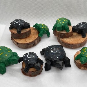 K&ouml;nnte beinhalten: Sieben h&ouml;lzerne Schildkr&ouml;tenfiguren mit einem Halbmond- und Sternenmuster. Die Schildkr&ouml;ten sind in Gr&uuml;n- und Schwarzt&ouml;nen bemalt und auf kleinen Holzscheiben ausgestellt.