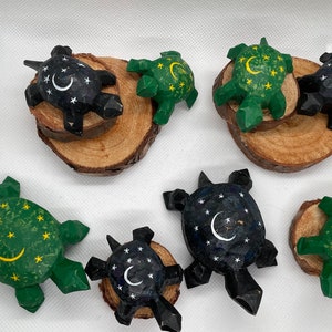 K&ouml;nnte beinhalten: Eine Sammlung von acht handgeschnitzten Holz-Schildkr&ouml;ten, jede mit einem anderen Design bemalt. Einige Schildkr&ouml;ten haben eine gr&uuml;ne Schale mit gelben Sternen und einem Halbmond, w&auml;hrend andere eine schwarze Schale mit wei&szlig;en Sternen und einem Halbmond haben.
