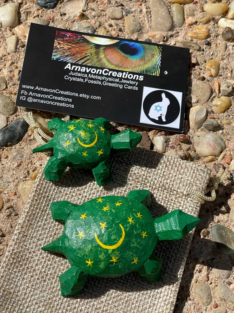 K&ouml;nnte beinhalten: Zwei h&ouml;lzerne Schildkr&ouml;tenfiguren, die gr&uuml;n mit gelben Sternen und einem Halbmond bemalt sind. Die Schildkr&ouml;ten stehen auf einer braunen Jutestoff-Oberfl&auml;che.