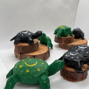 K&ouml;nnte beinhalten: F&uuml;nf h&ouml;lzerne Schildkr&ouml;tenfiguren, in Schwarz und Gr&uuml;n bemalt mit wei&szlig;en und gelben Sternen und Halbmonden. Die Schildkr&ouml;ten sitzen auf kleinen Holzscheiben.